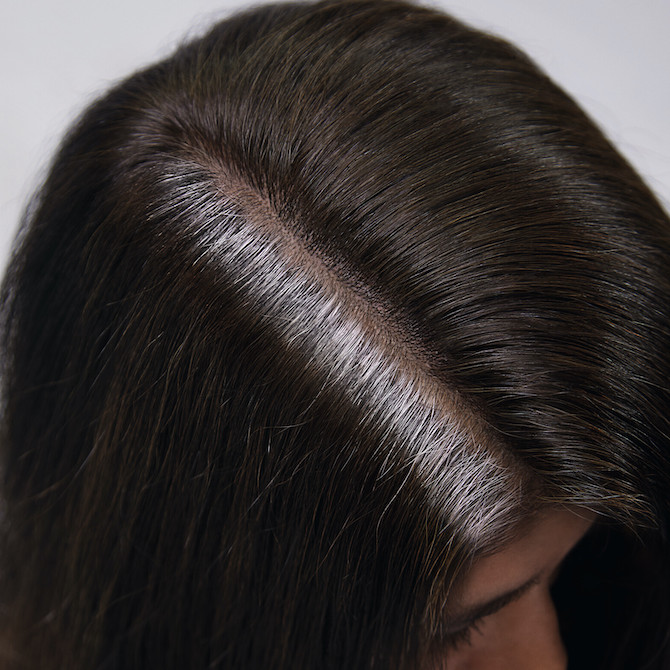 Top of woman’s head with brunette hair and stubborn gray roots. 
