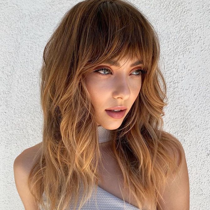 Model with long, wavy, light brown hair and bottleneck bangs.