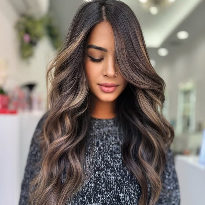 Model with long, loosely curled, brunette hair featuring caramel balayage.