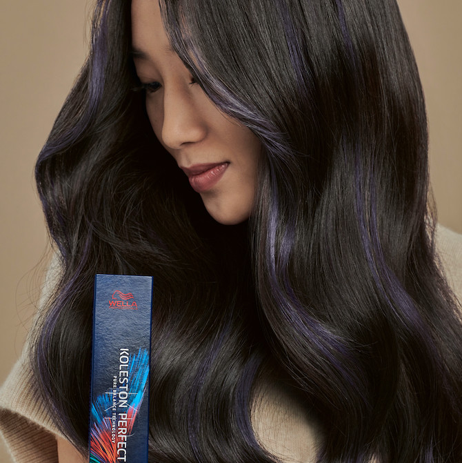 model with long, black hair looks to the side whilst holding a box of Koleston Perfect by Wella Professionals