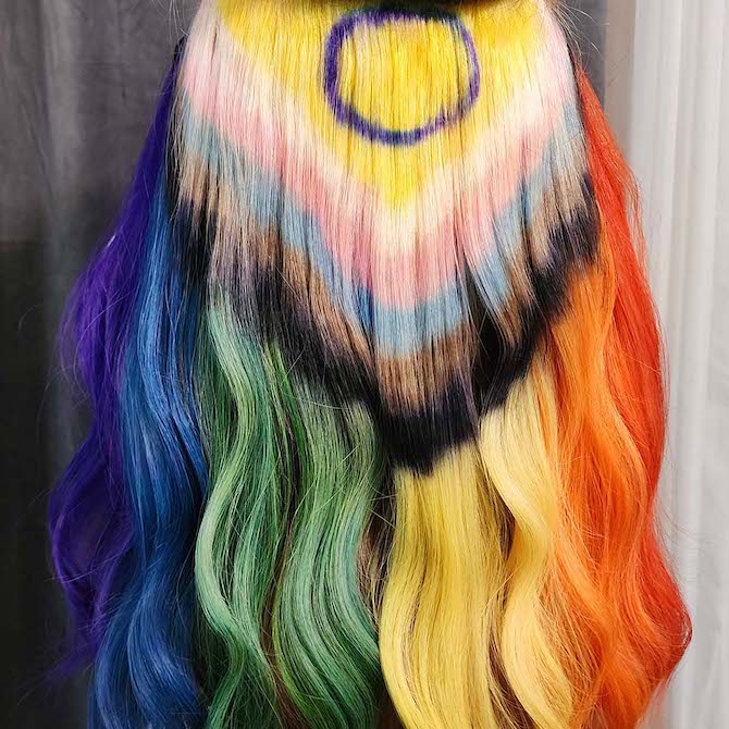 Back of model’s head, the Progress Pride flag has been painted through their long, straight hair.