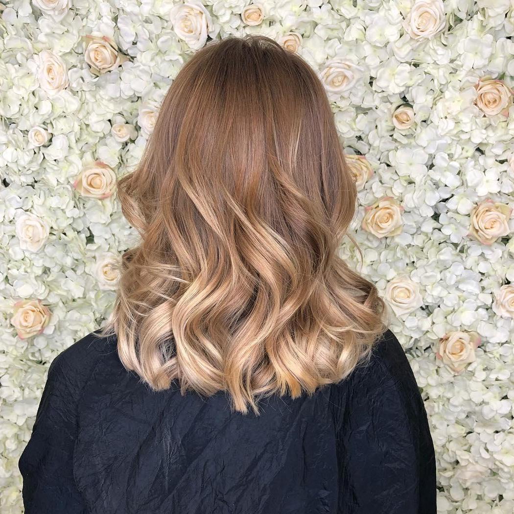 Woman with mid length, dirty blonde, balayage hair styled with loose waves