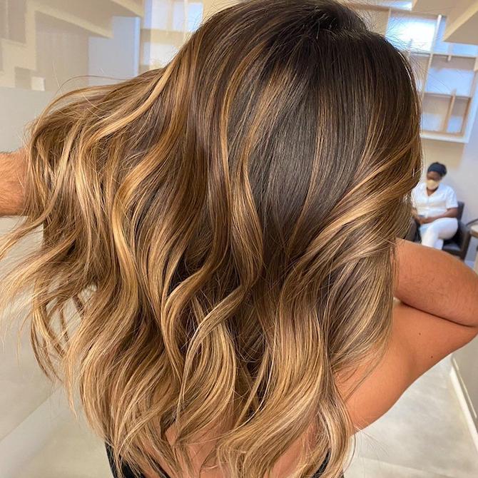 Frau mit langem, gewelltem, braunem Haar und karamellfarbener Balayage, kreiert mit Wella Professionals. 