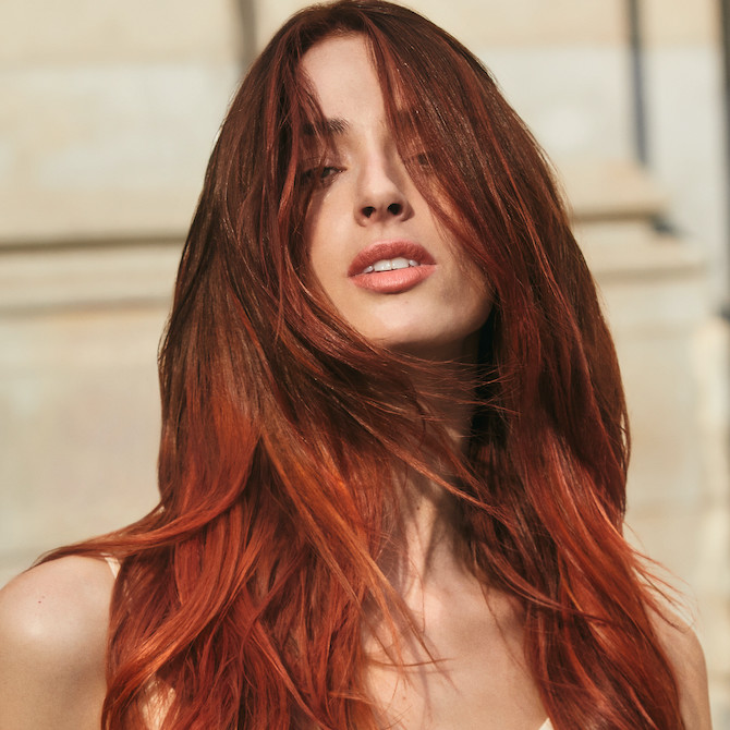 Model with long, tousled, red hair faces the camera.