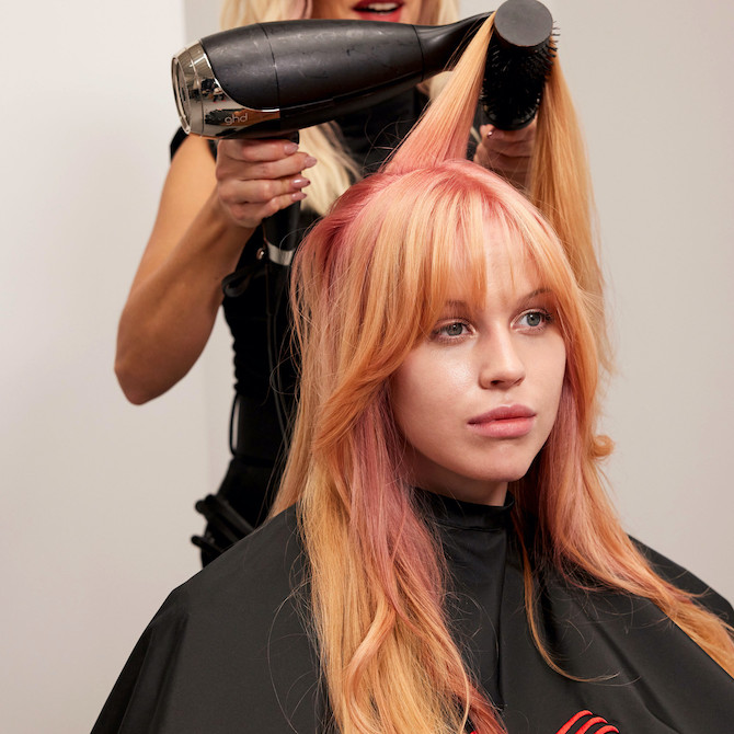 Model has their long, pink and blonde hair blow-dried by a stylist.