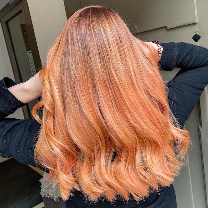 Back of woman’s head with long, wavy blorange hair. 