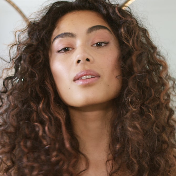 Woman with dark brown, curly hair faces the camera.