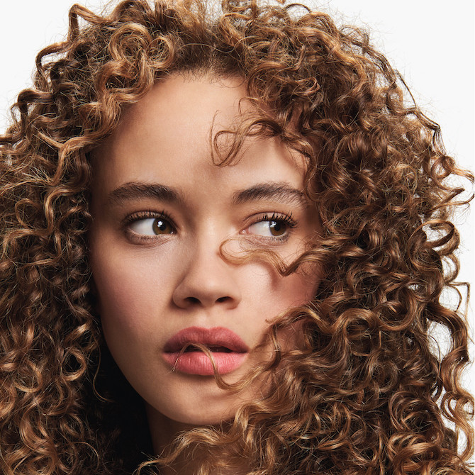 Model with thick, curly, brown hair faces the camera.