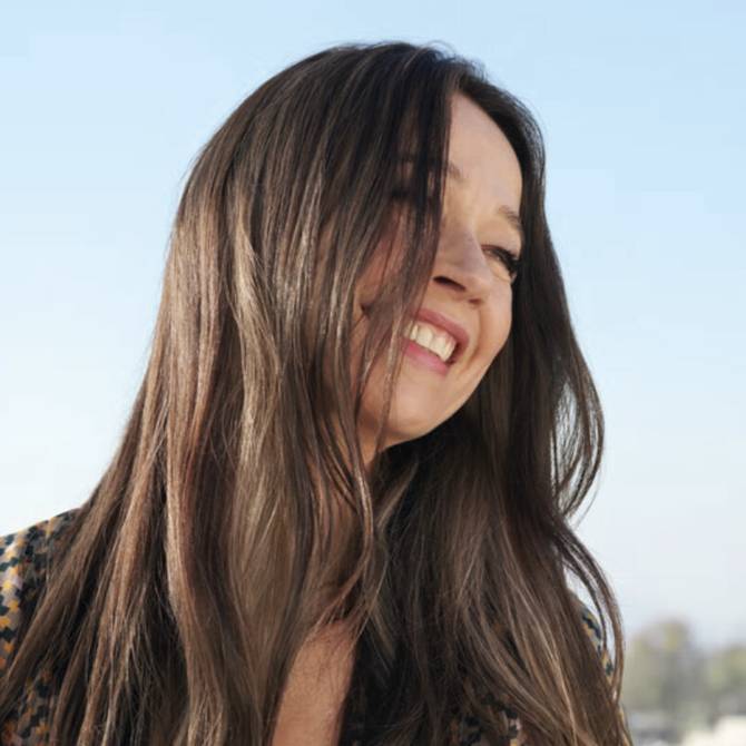 Model with dark brown hair, smiling and gazing off into the distance.
