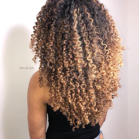 Back of woman’s head with blonde balayage through curly hair, created using Wella Professionals