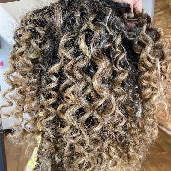 Side profile of woman with beachy blonde curly hair, created using Wella Professionals.