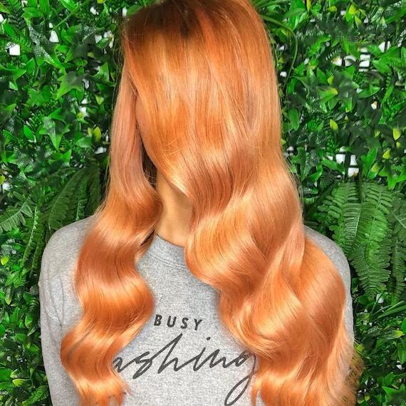 Woman with long, glossy, peachy-blorange hair falling past her shoulders.