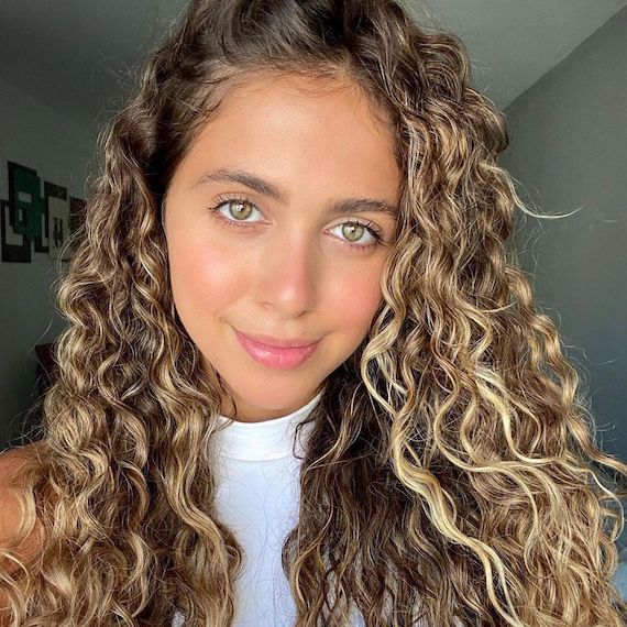Person with type 2C curly hair and blonde highlights takes a selfie 