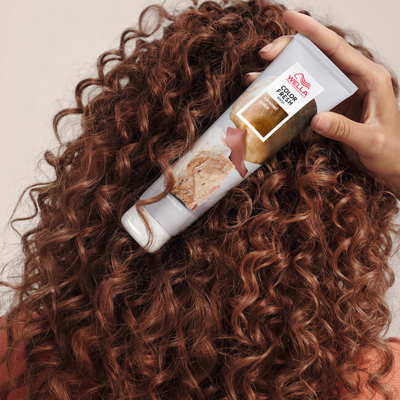 Model with brown, curly hair holds up a tube of Color Fresh Mask in Caramel Glaze. 