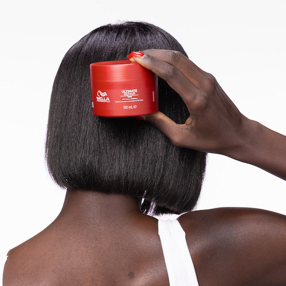 Model with short, dark brown hair holds up a tub of ULTIMATE REPAIR Mask.