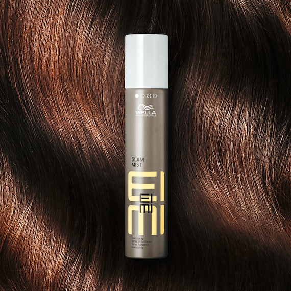 EIMI Glam Mist in front of a model’s shiny, brunette hair.