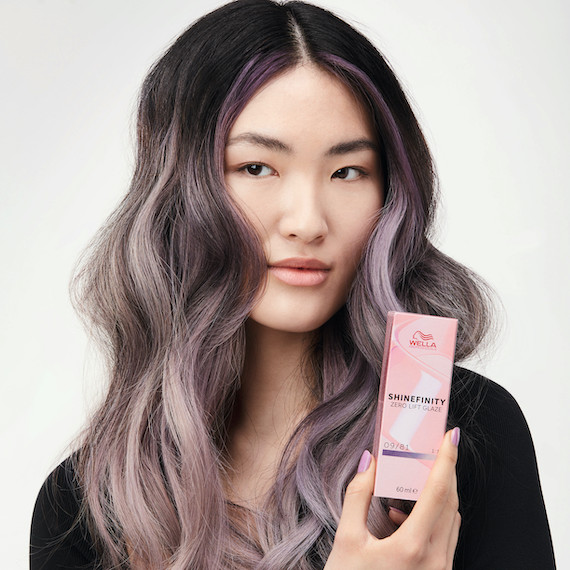 Model with dark hair and violet-blonde ends holds a box of Shinefinity by Wella Professionals 