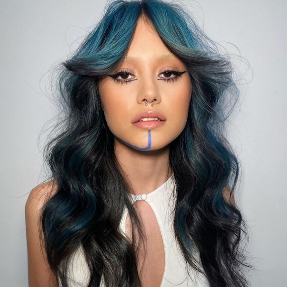 Model with long, black hair and blue highlighted bangs faces the camera.