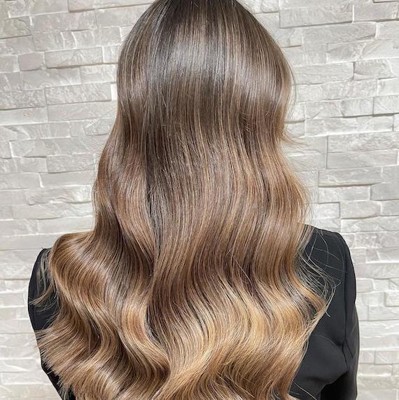 Back of woman’s head with long, loosely waved, bronde hair and dark blonde balayage.