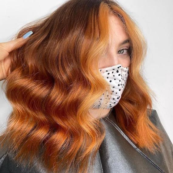 Woman faces camera with wavy copper hair and a strawberry blonde money-piece.