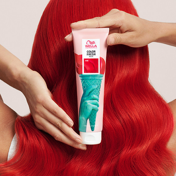 A person with bright red hair holding a bottle of Wella Professional Color Fresh Mask behind their head