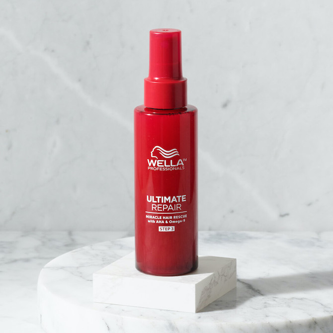 A red bottle of Ultimate Repair Miracle Hair Rescue treatment stood against a gray marble wall 