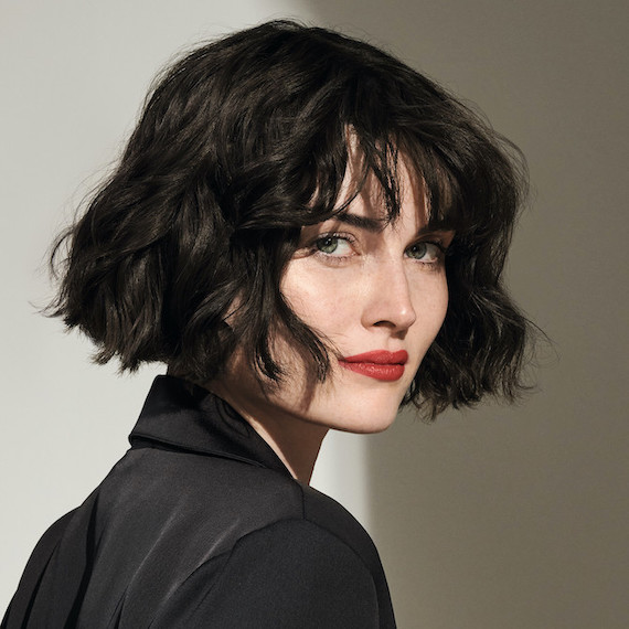 Model with black, wavy bob haircut and fringe faces the camera.