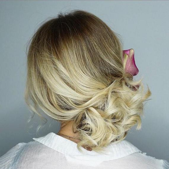 Back of woman’s head with blonde ombre hair styled in a loose updo. 