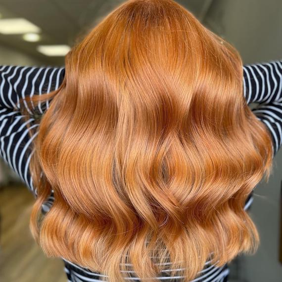 Back of woman’s head with long, wavy, blorange hair. 