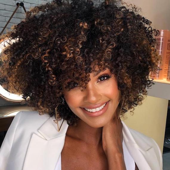 Woman smiles at the camera with curly, iced caramel espresso hair colour.