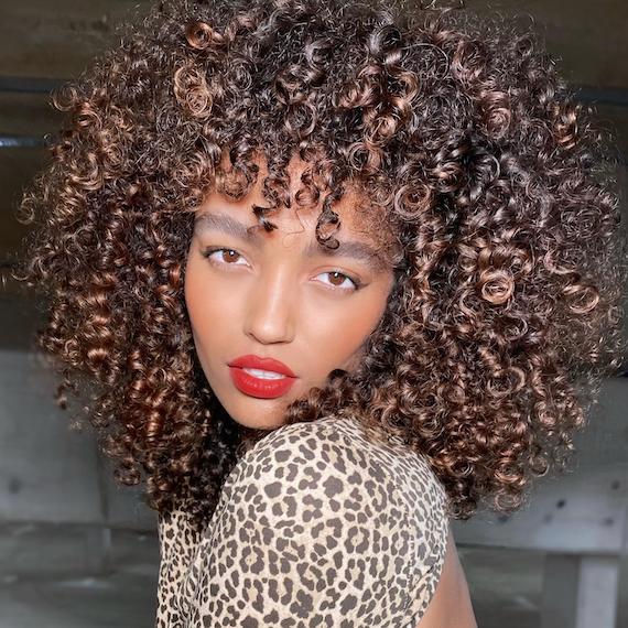 Woman faces the camera with curly, bronzy brown hair.