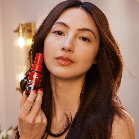 Model with dark brown hair holds up ULTIMATE REPAIR Night Serum.