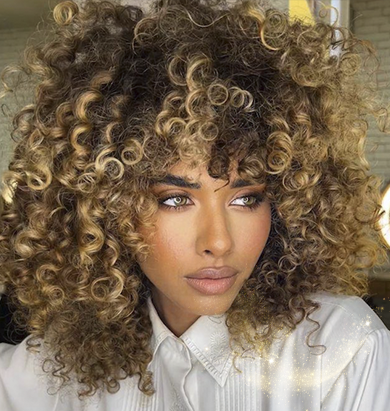 Model with warm brown, glossy, curly hair featuring caramel balayage.