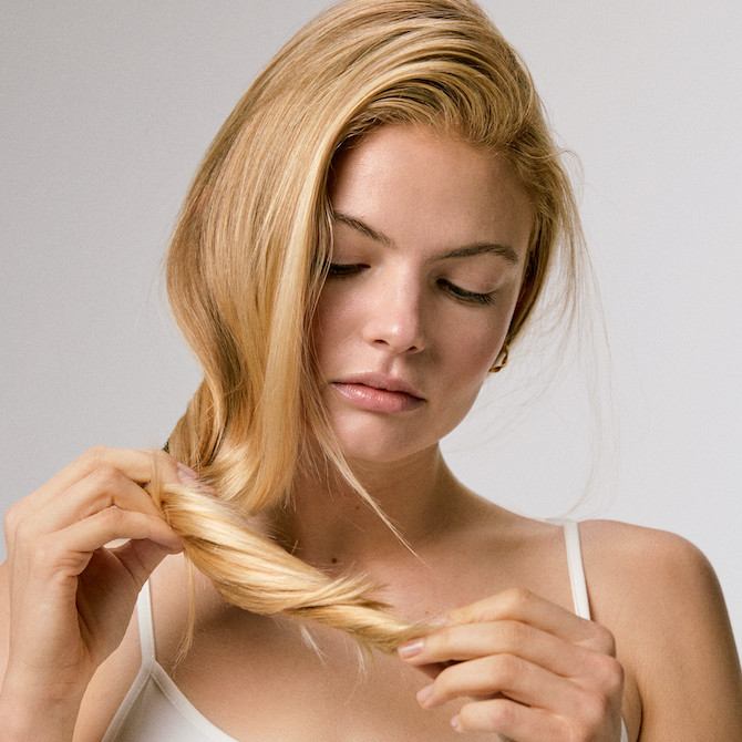 Model looks at the ends of their blonde hair.