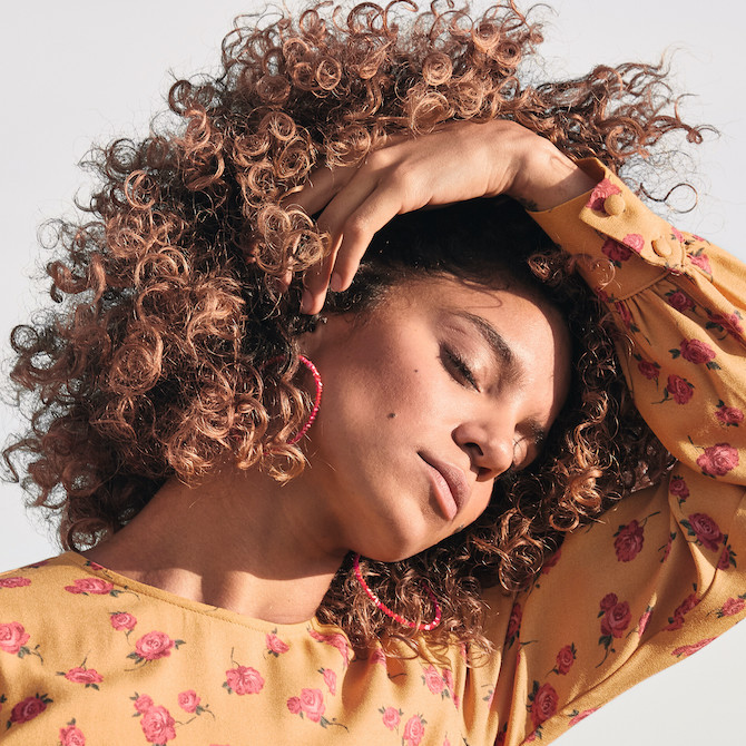 model with light brown curly hair sweeps her locks away from her eyes.