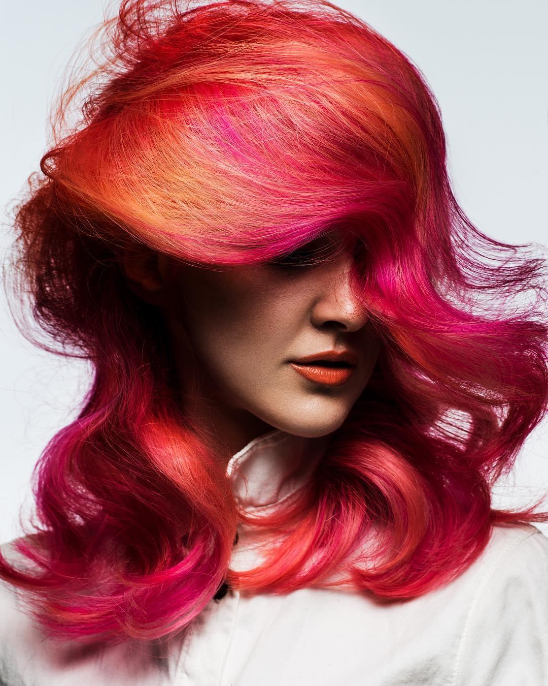 Woman with bright orange red pink hair, styled with loose waves