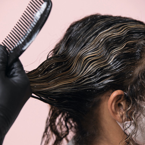 Seitenprofil einer Frau, während Farbe mithilfe eines Kammes auf ihr Haar aufgetragen wird.