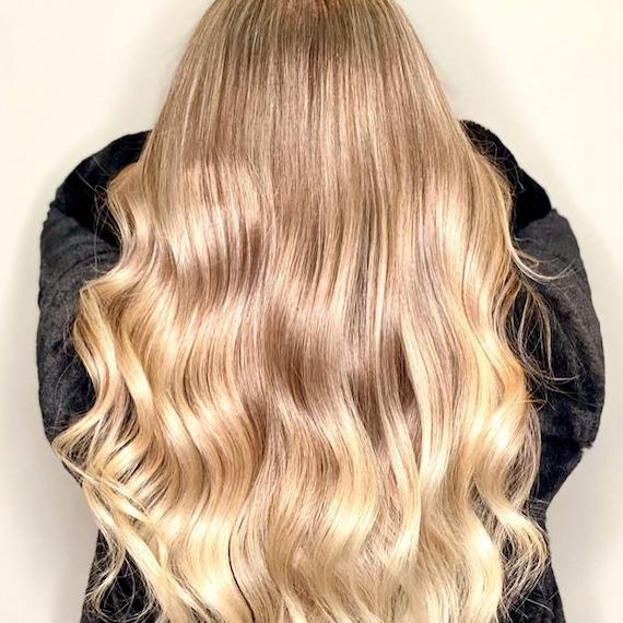 Back of woman’s head with long, sunlight blonde hair in loose curls, created using Wella Professionals. 