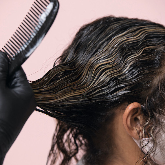 Side profile of woman as colour is applied to her hair with a comb.