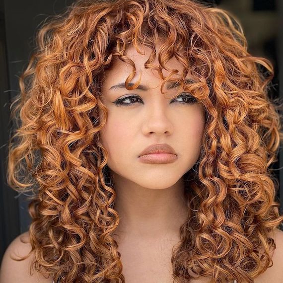 Model with long, curly amber brown hair looks out into the distance.