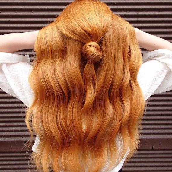 Back of model’s head. She lifts her amber blonde hair which is styled in a half up half down do.