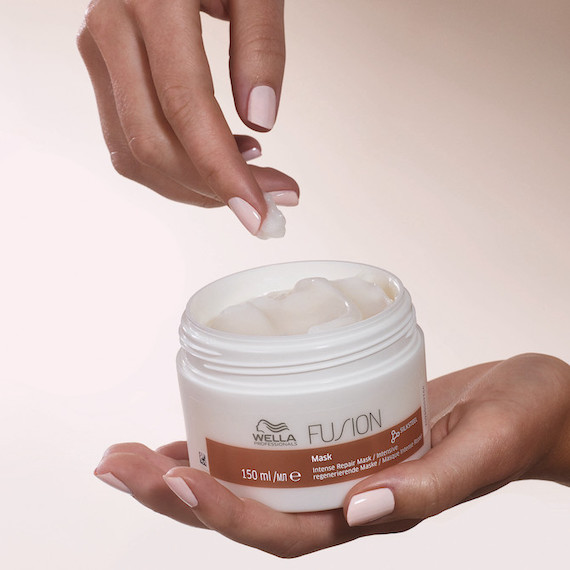 Close-up of hand holding an open pot of Fusion Intense Repair Hair Mask by Wella Professionals.