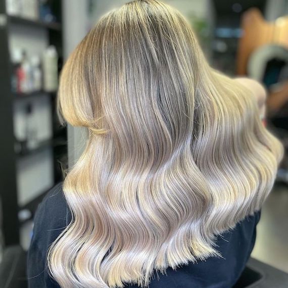 Back of model’s head with shiny, wavy, light ash blonde ombre hair.