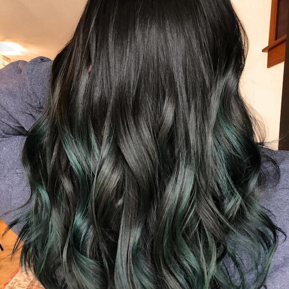 Back of woman’s head with long, wavy, dark brunette hair and ash green balayage