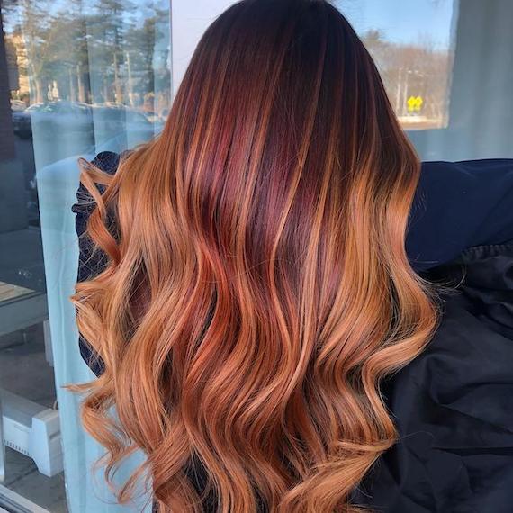 Back of woman’s head with long, glossy, auburn hair and blonde balayage. 