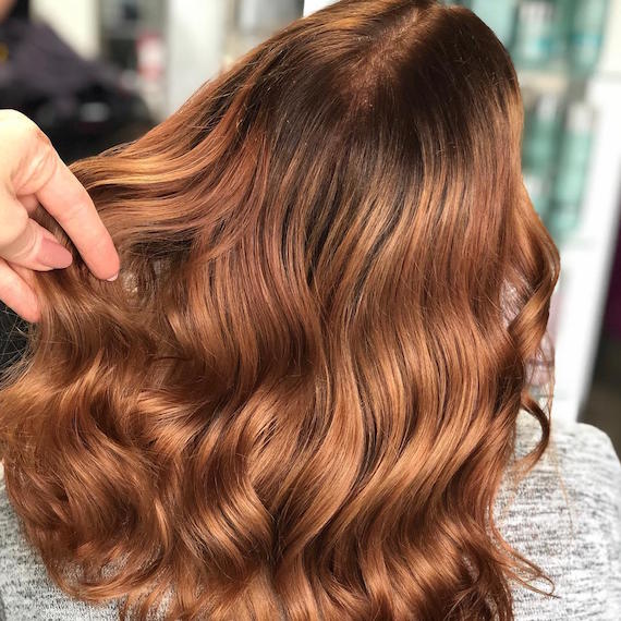 Back of woman’s head with mid-length, wavy, light auburn hair, created using Wella Profes-sionals.