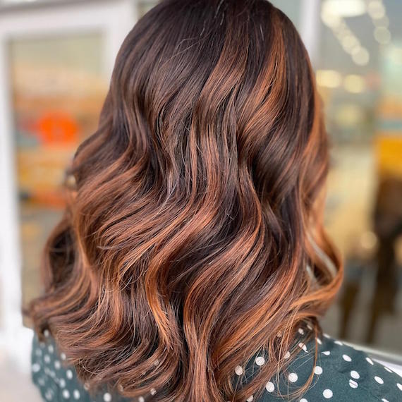 Back of woman’s head with wavy, brown hair and auburn highlights, created using Wella Professionals.