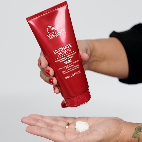 A red bottle of Ultimate Repair Conditioner is being squeezed into the palm of a hand