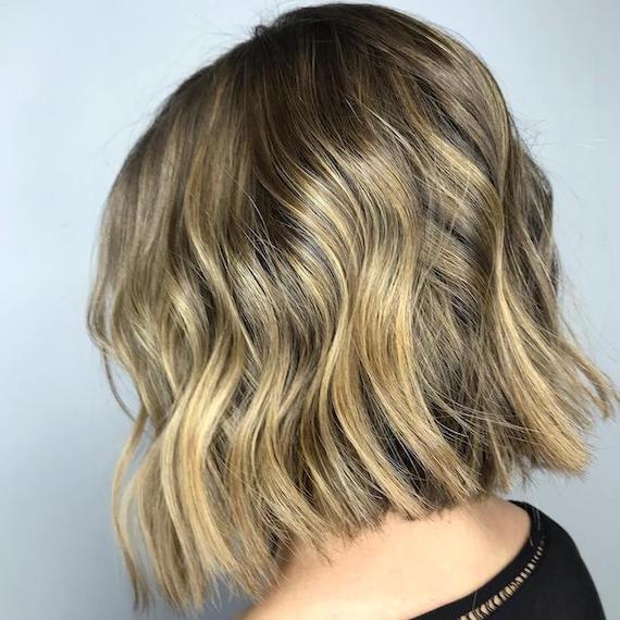Side profile of woman with dirty blonde balayage through a wavy bob, created using Wella Professionals.
