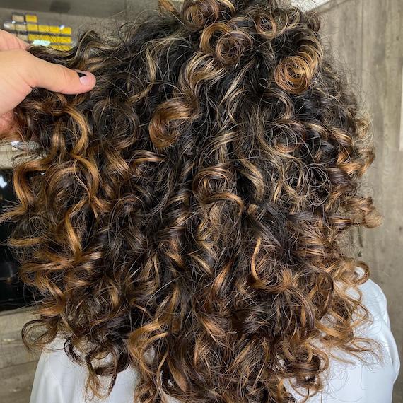 Back of woman’s head with dark brown curly hair and chunky, caramel blonde balayage, created using Wella Professionals.